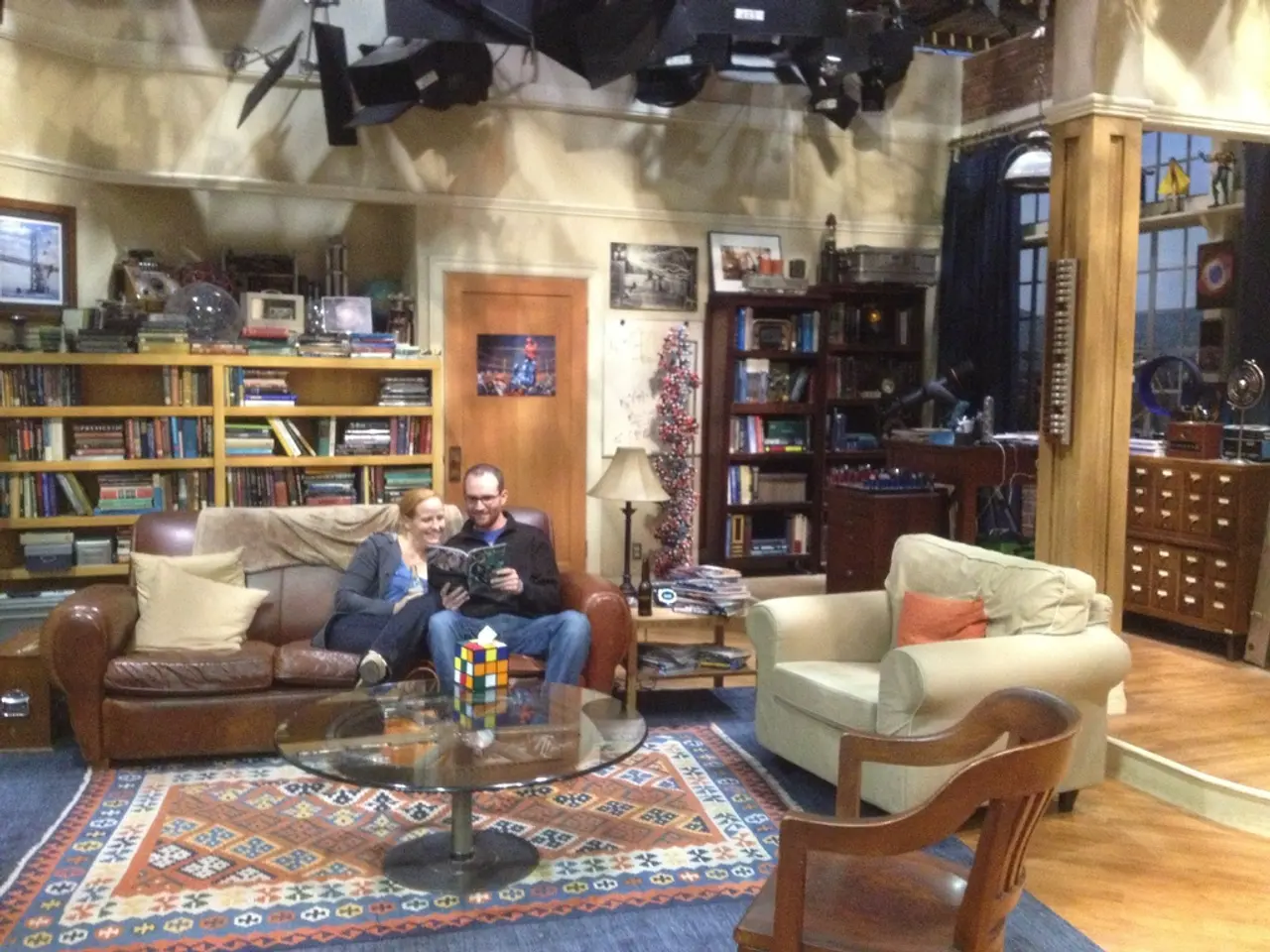 There are sitting in a room. They are sitting in a sofa. He is holding book. She is look at the...