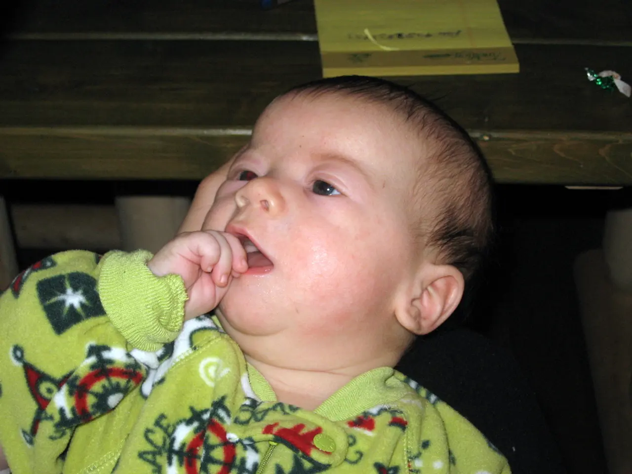 In this picture there is a baby wearing green dress and there is a table behind her which has a...