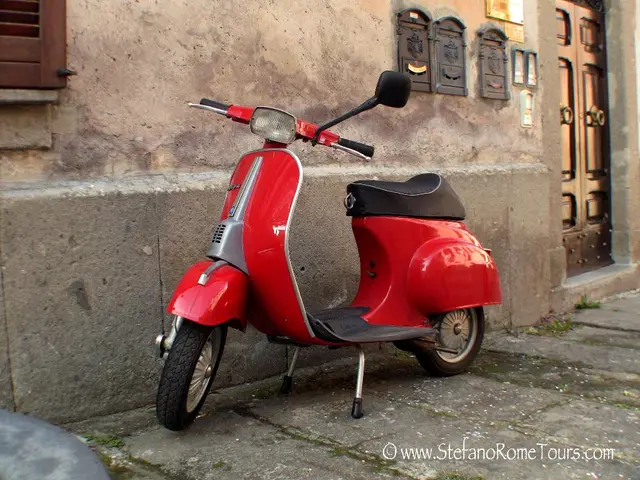 In the center of the image there is a red color scooter. In the background of the image there is a...