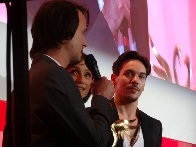 In this image, we can see people standing and are wearing coats, one of them is holding a mic and...